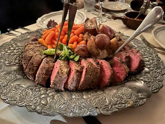 Sliced Chateaubriand on an ornate silver platter with carrots and roasted potatoes